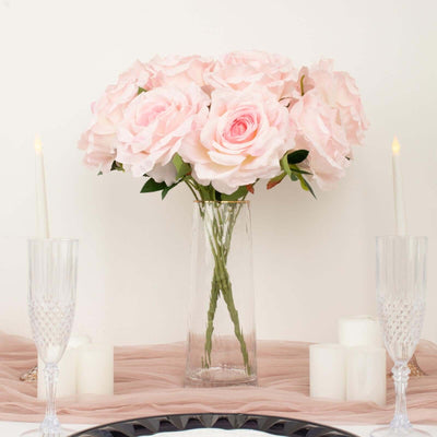 Pink roses in a clear vase with candles on a table setting.