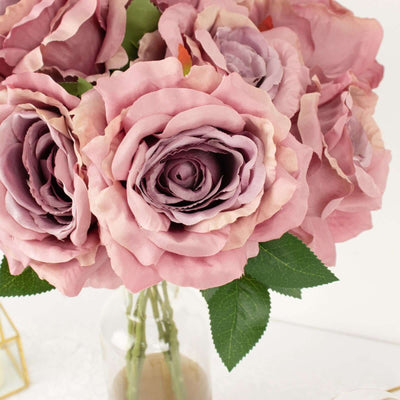 Pink silk rose bouquet with green leaves in a glass vase.