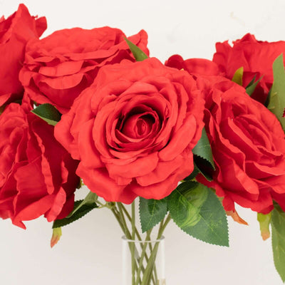 Red artificial roses in a clear vase against a white background.