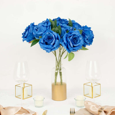 Blue artificial roses in a glass vase on a dining table.