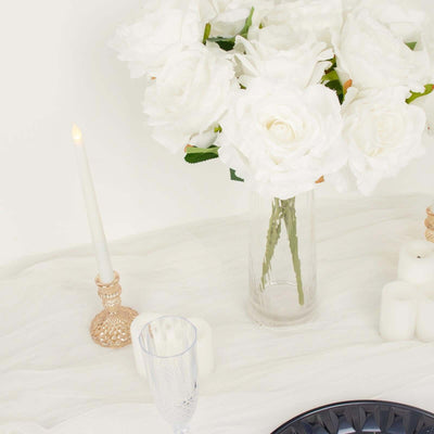 White roses in a clear vase with candles and elegant tableware.