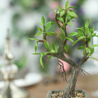 Artificial bonsai tree in a decorative pot, showcasing vibrant green leaves.