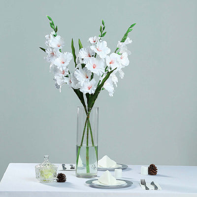 White artificial flowers in a clear vase on a table setting with elegant decor.