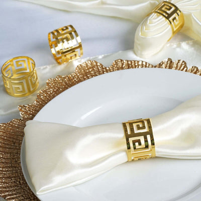 Elegant gold napkin rings on a white plate with silk napkins and a textured table runner.
