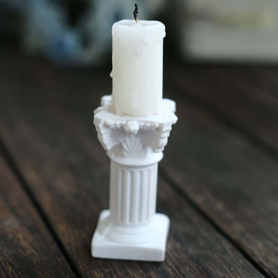 White candle on a decorative pillar holder, featuring intricate detailing.