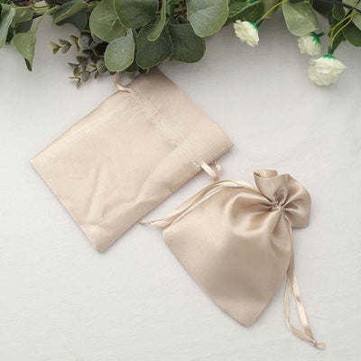 Beige satin drawstring bags on a soft surface with greenery and flowers.