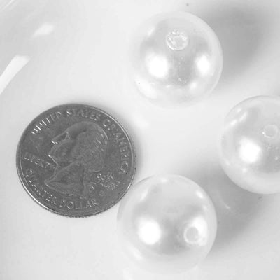 Three clear plastic beads next to a quarter on a white background.