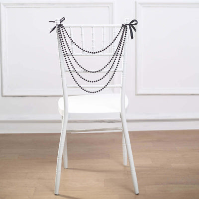 Black beaded garland draped over a white chair with ribbons.