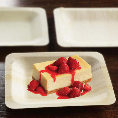 Cheesecake slice topped with strawberries and sauce on a biodegradable plate.