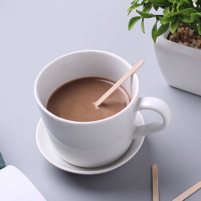 White coffee cup with brown coffee and wooden stirrer on a gray surface.
