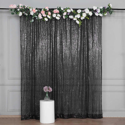 Black sequin backdrop with floral decoration and a white pedestal vase.