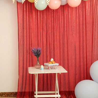 Decorative party setup with a table, balloons, and a shimmering red backdrop.