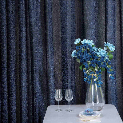 Elegant blue floral arrangement with glasses on a table against shimmering dark curtains.