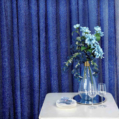 Elegant blue floral arrangement in a glass vase on a white table with dinnerware.