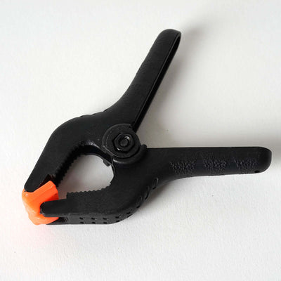 Black plastic clamp with orange tips on a plain background.