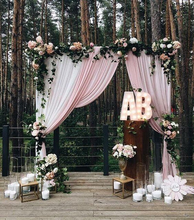 Wedding arch with drapes and flowers in a forest setting.