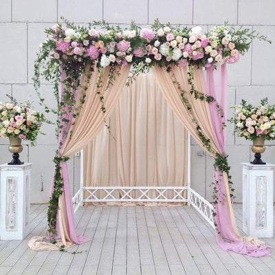 Elegant floral wedding arch with draped fabric and decorative columns.