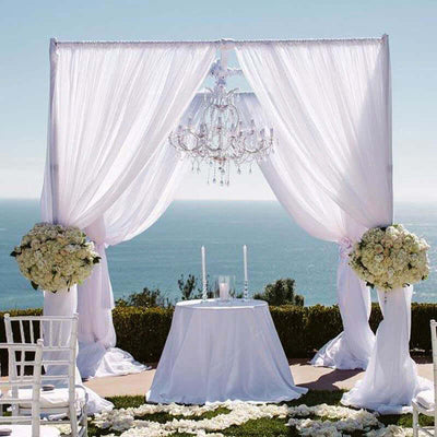 Elegant wedding altar with draped white fabric and chandelier overlooking the ocean.