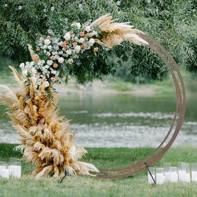 Floral arch with pampas grass and candles by a serene water backdrop.