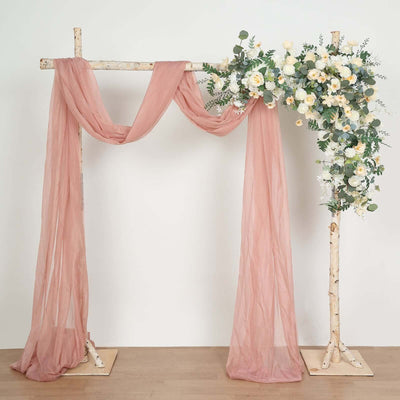 Floral arch with draped fabric in soft pink and greenery accents.