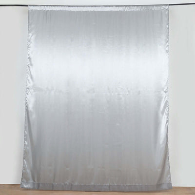 Silver satin curtain panel hanging against a neutral backdrop.