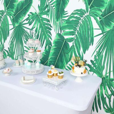 Dessert table with cupcakes and cake against a tropical leaf backdrop.