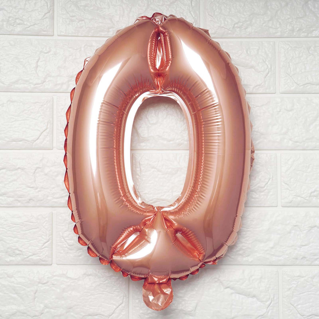Rose gold number zero balloon on a textured white wall.
