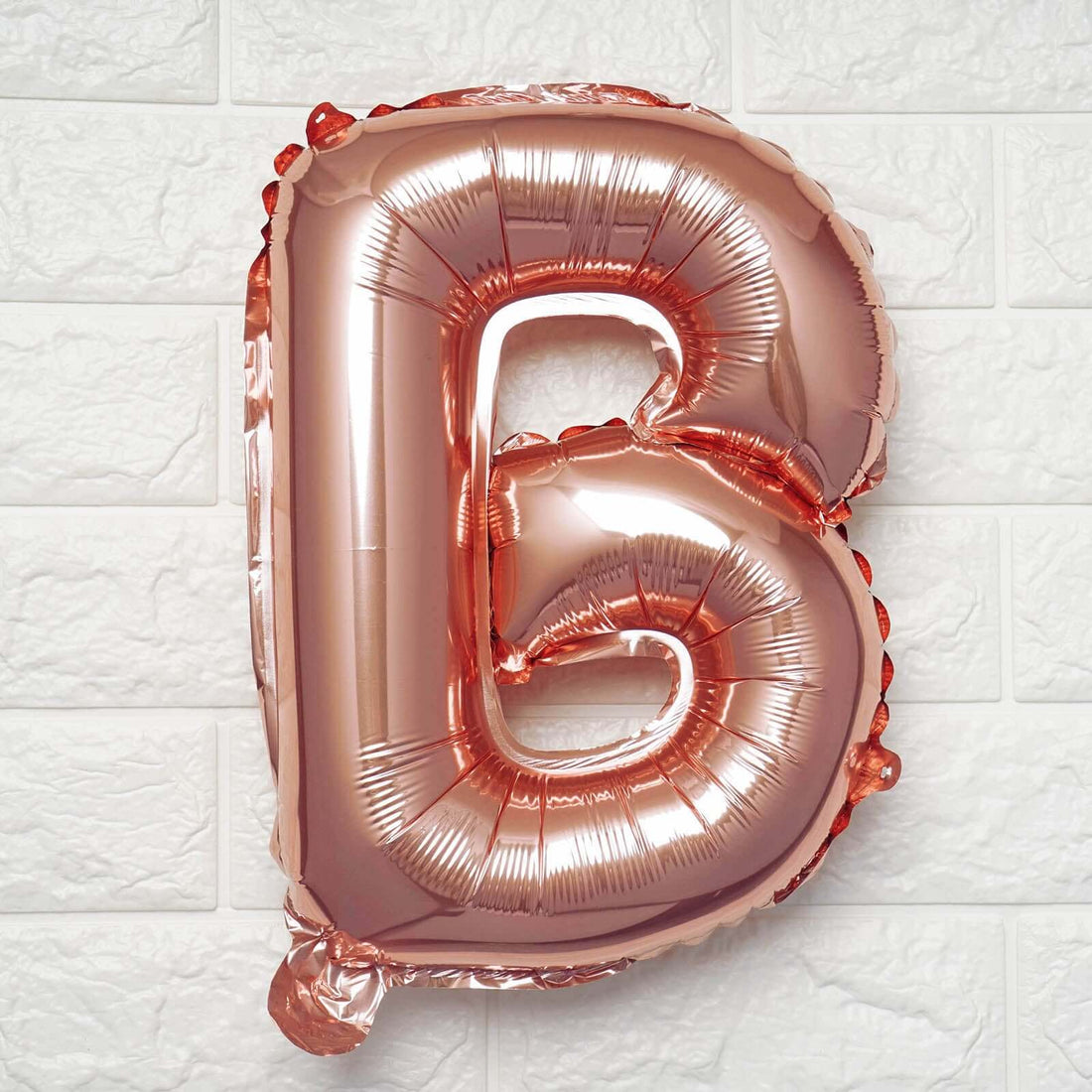 Rose gold foil letter B balloon on a textured white wall.