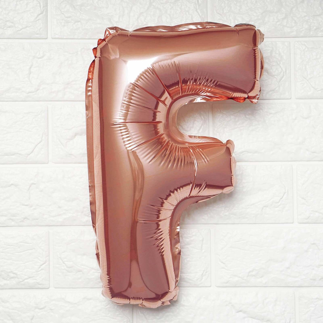 Rose gold letter F balloon on a plain background.