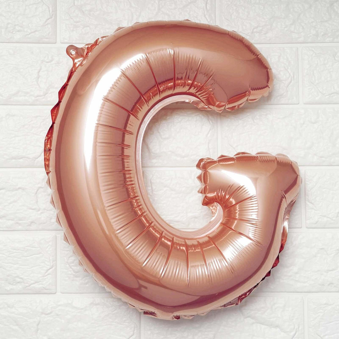 Rose gold letter G balloon on a textured white background.