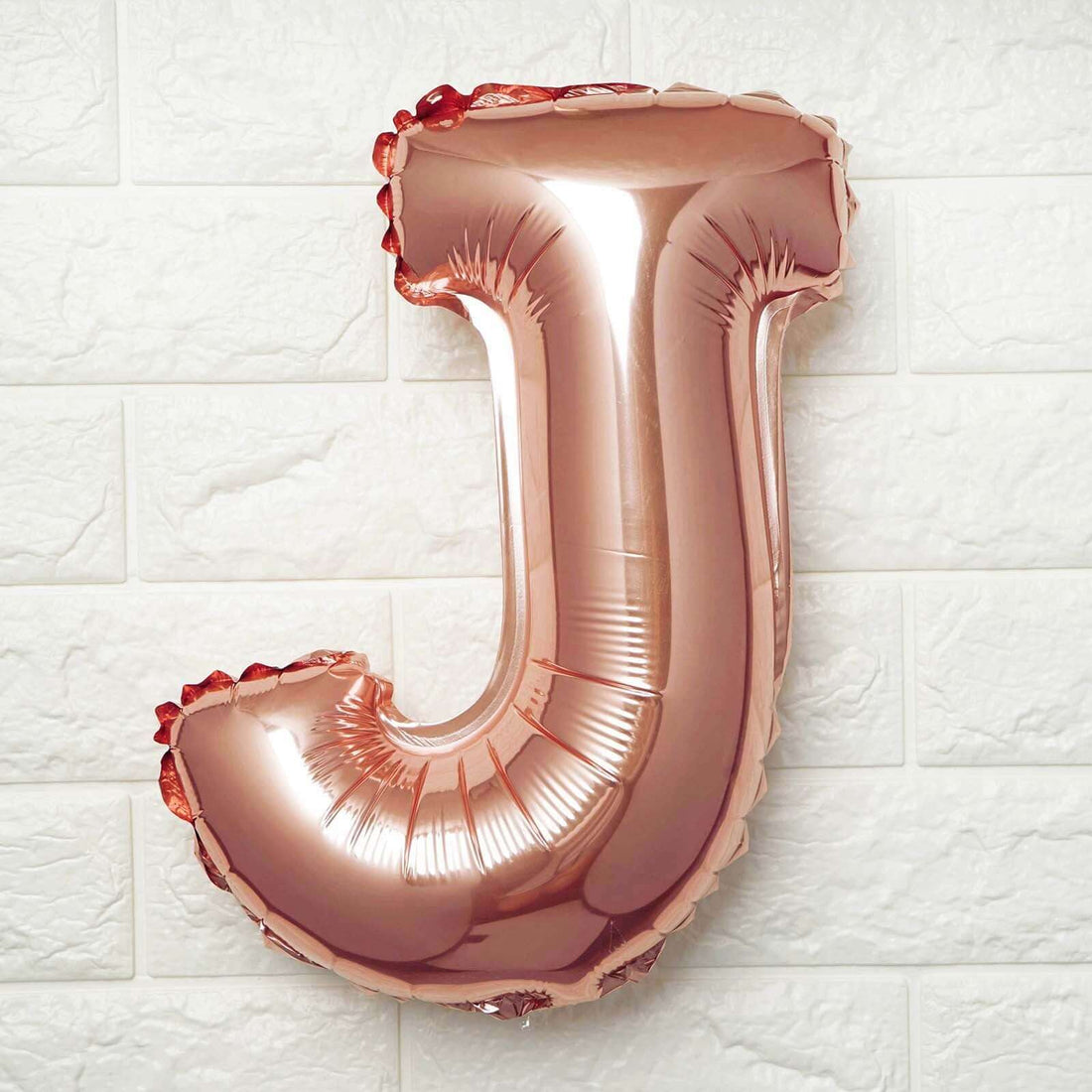 Rose gold foil letter J balloon on a textured wall.