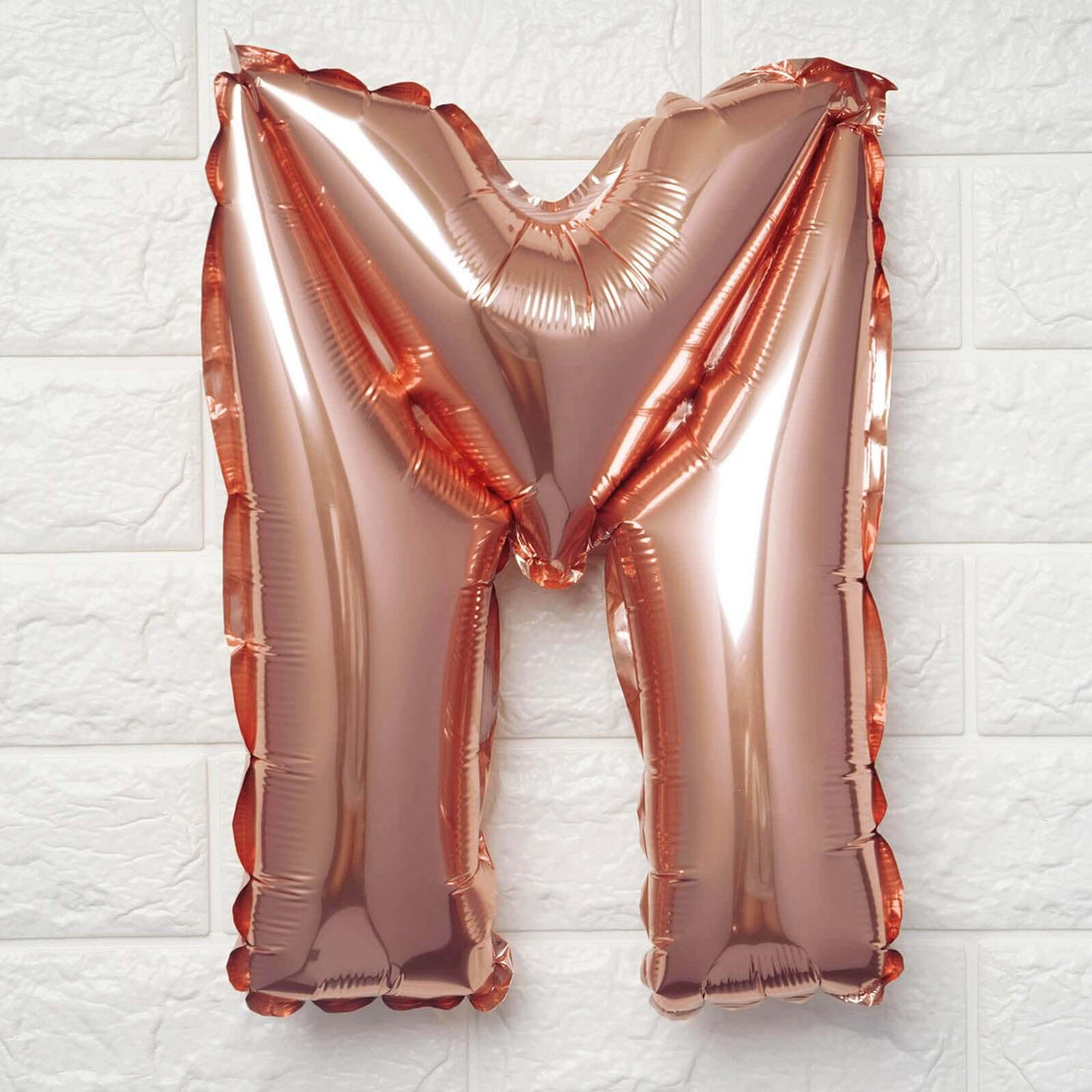 Rose gold letter M balloon on a white background.