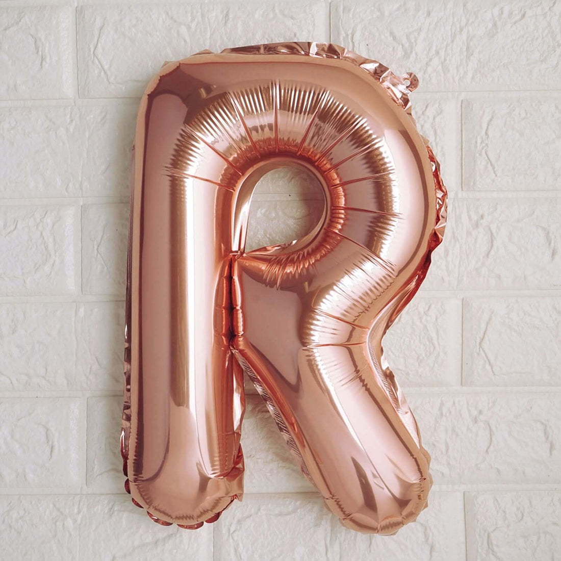 Rose gold foil letter "R" balloon on textured white wall.