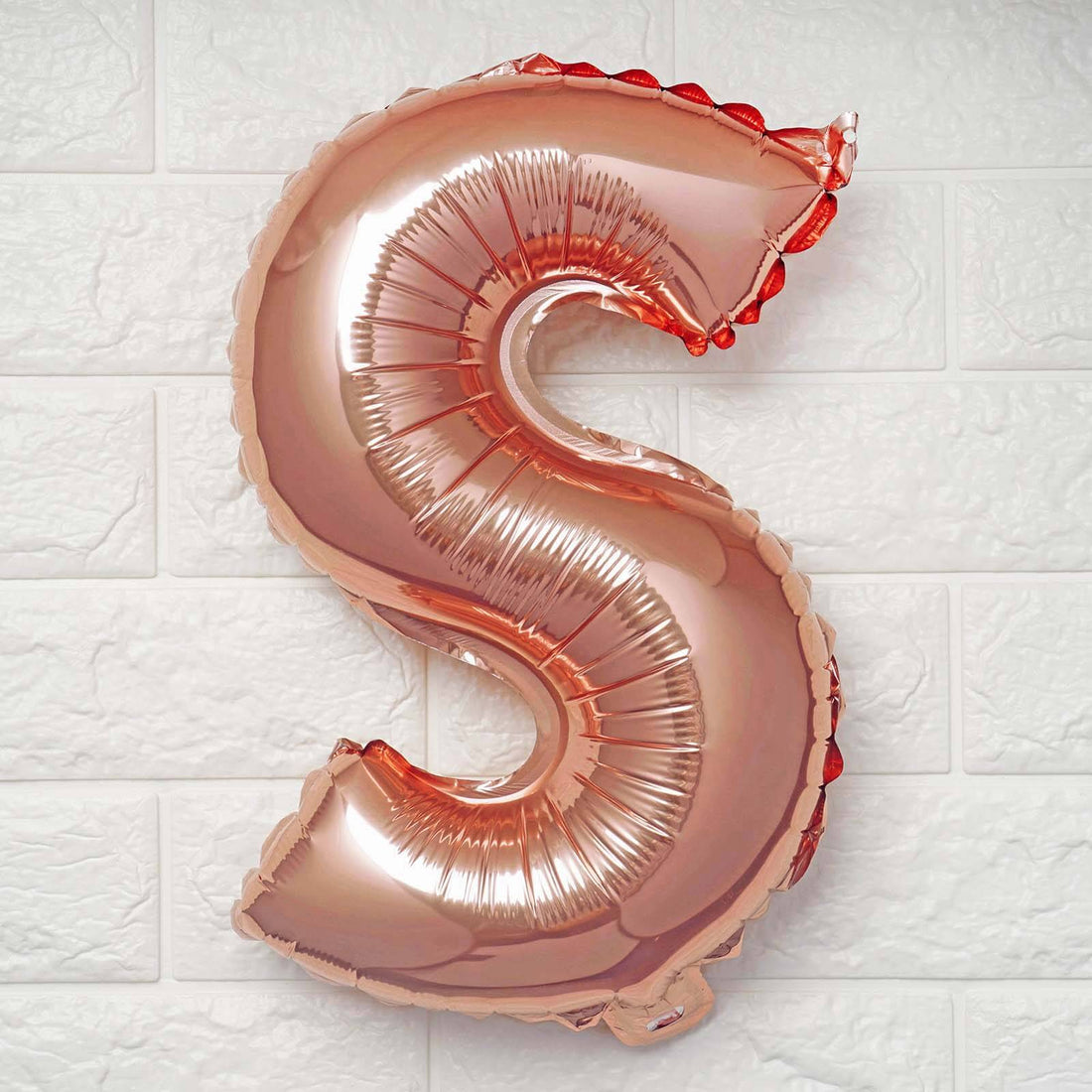Rose gold letter S balloon on a plain background.