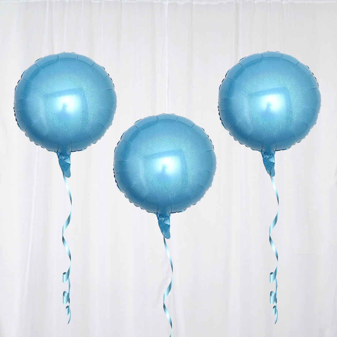 Three blue helium balloons with ribbons against a plain background.