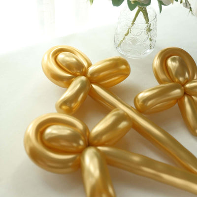 Gold balloon decorations in stylish ribbon shapes on a light surface.