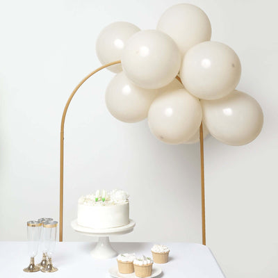 Party decor featuring a cake, cupcakes, and balloon arch on a table.