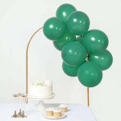 Green balloons arching over a cake and cupcakes on a table.