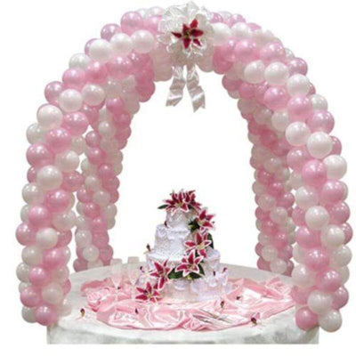 Pink and white balloon arch with a decorated cake and flowers for a celebration.