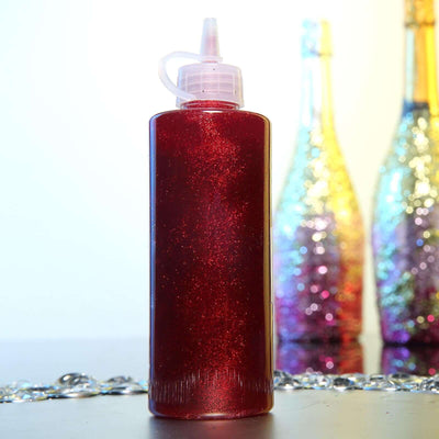 Red glitter glue bottle on a shiny surface with sparkling bottles in the background.