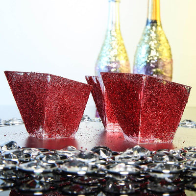 Red glitter party cups on a reflective surface with sparkling decorations.