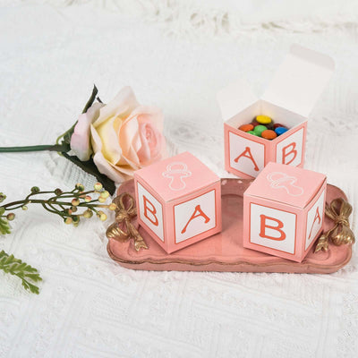 Pink baby blocks with candy and a rose on a decorative tray.