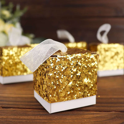 Gold glitter gift box with a white ribbon on a wooden surface.