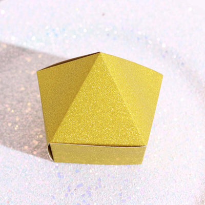 Gold glitter pyramid gift box on a shimmering surface.