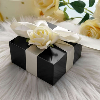 Black gift box with white ribbon and rose on a fluffy surface.