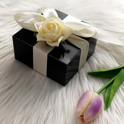 Black gift box with white ribbon and rose on soft fur background.
