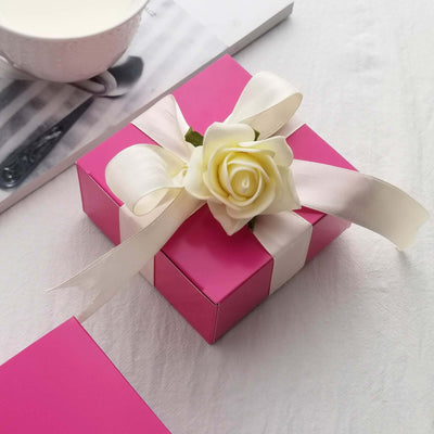 Pink gift box with a white ribbon and rose decoration.