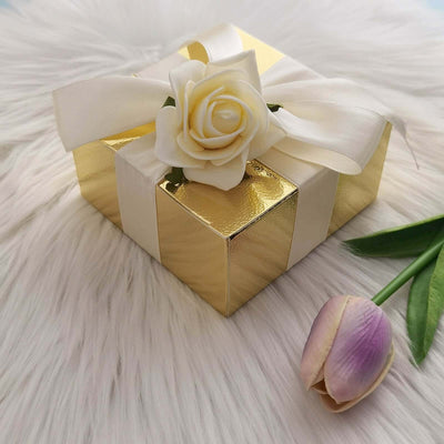 Gold gift box adorned with a rose and ribbon on a soft white fur surface.