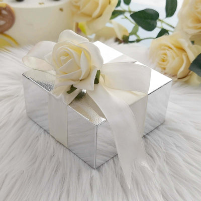 Silver gift box with a white ribbon and rose decoration on a soft white surface.