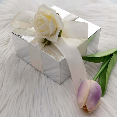 Silver gift box adorned with a white rose and ribbon, next to a tulip.